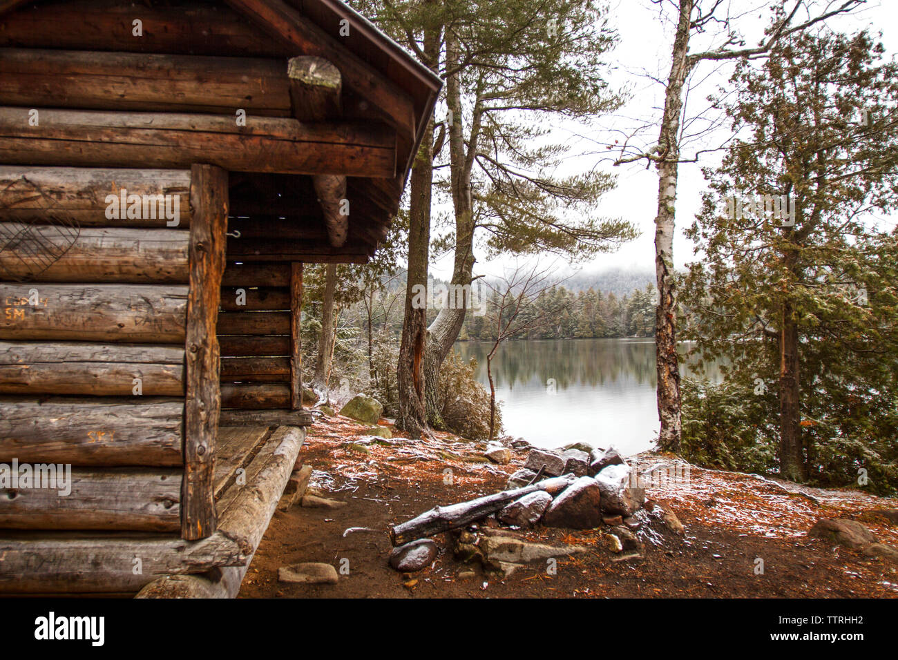 Old log cabin by lake and trees in forest Stock Photo