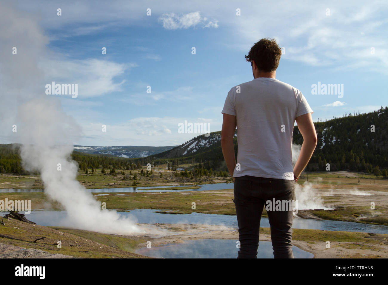 Rear view of hiker looking at steam coming out from hot springs at Yellowstone National Park against sky Stock Photo