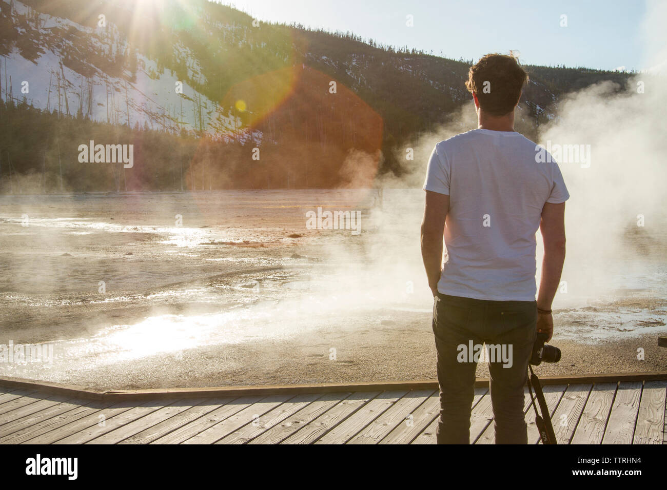 Rear view of hiker looking at steam coming out from hot spring at Yellowstone National Park Stock Photo