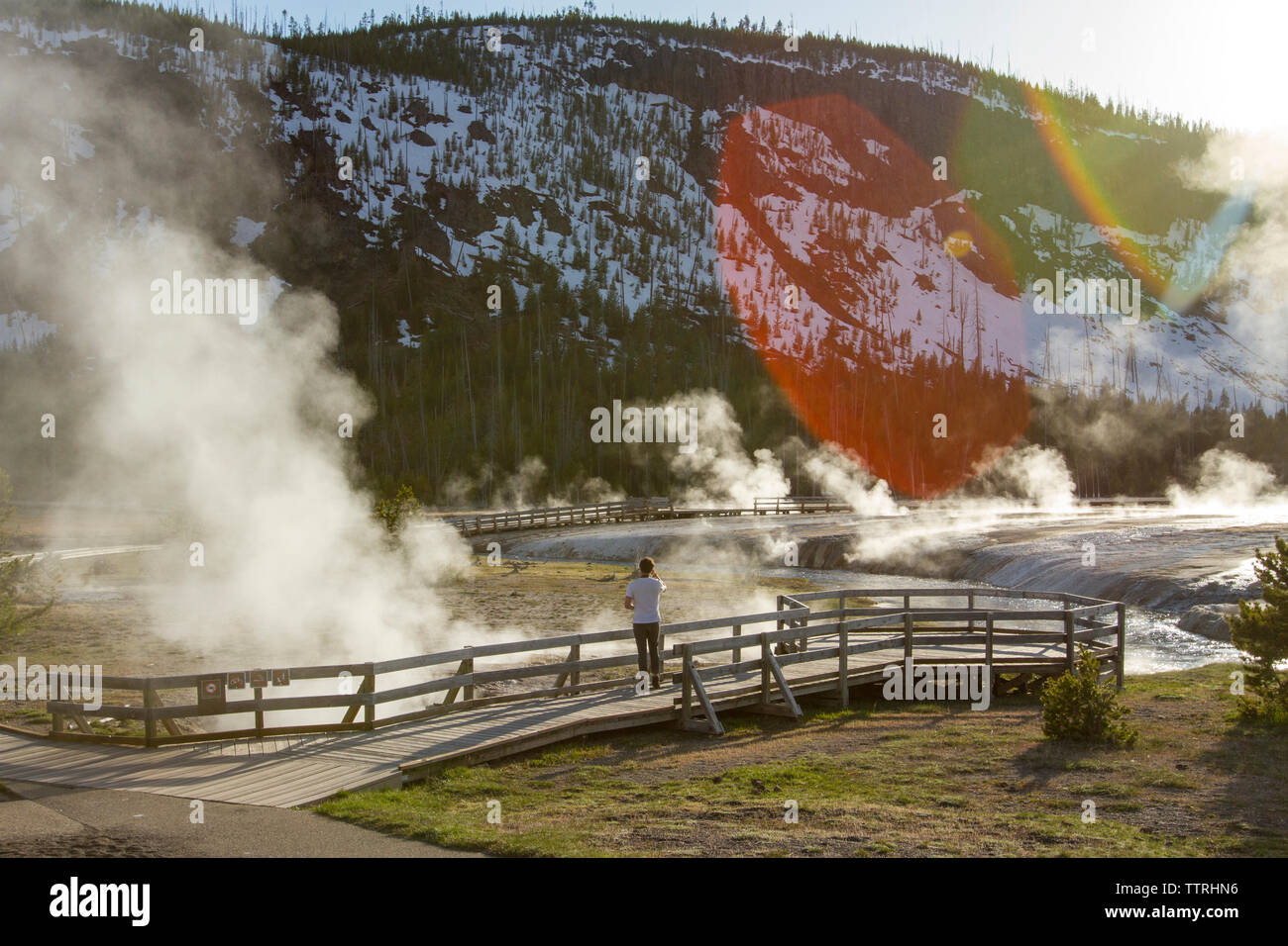 Mid distance of hiker looking at steam coming out from hot spring at Yellowstone National Park Stock Photo