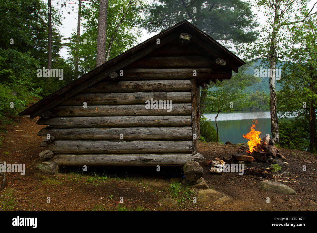 Campfire by log cabin in forest Stock Photo