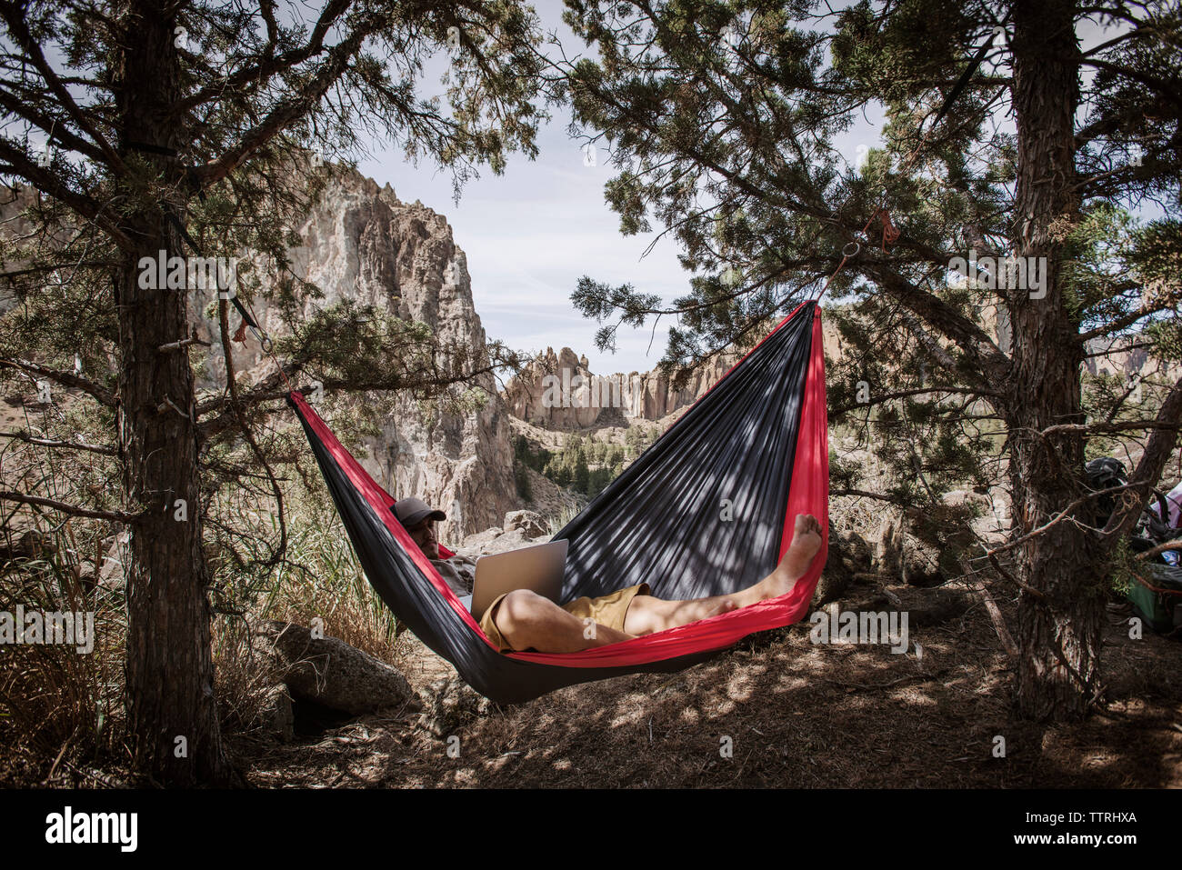 Man using laptop while resting in hammock over field in mountain Stock Photo