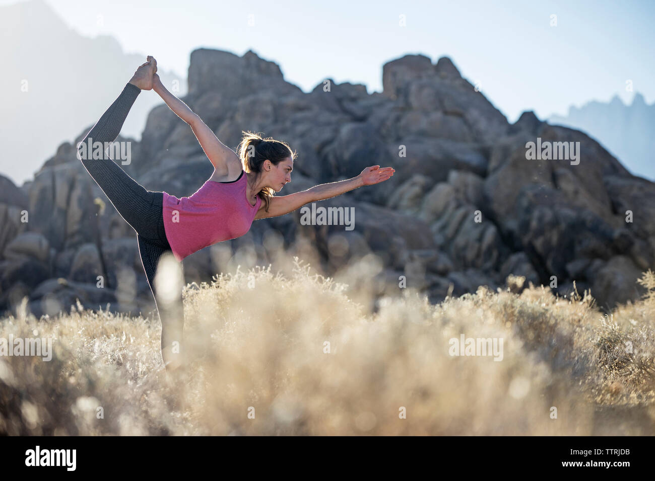 Woman standing on one leg while practicing yoga on field against mountains Stock Photo