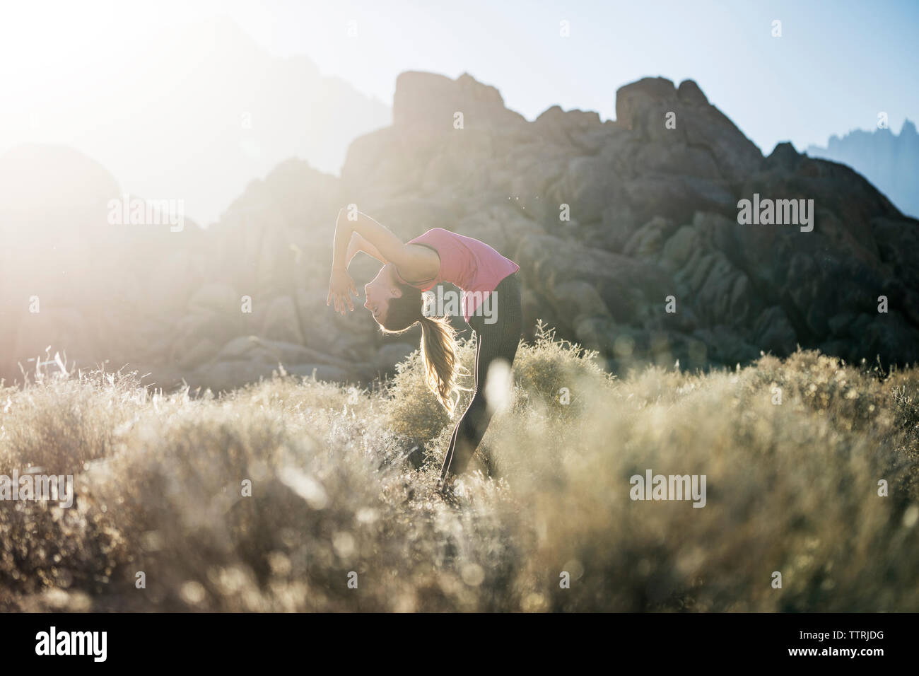 Woman practicing yoga on field against mountains during sunny day Stock Photo
