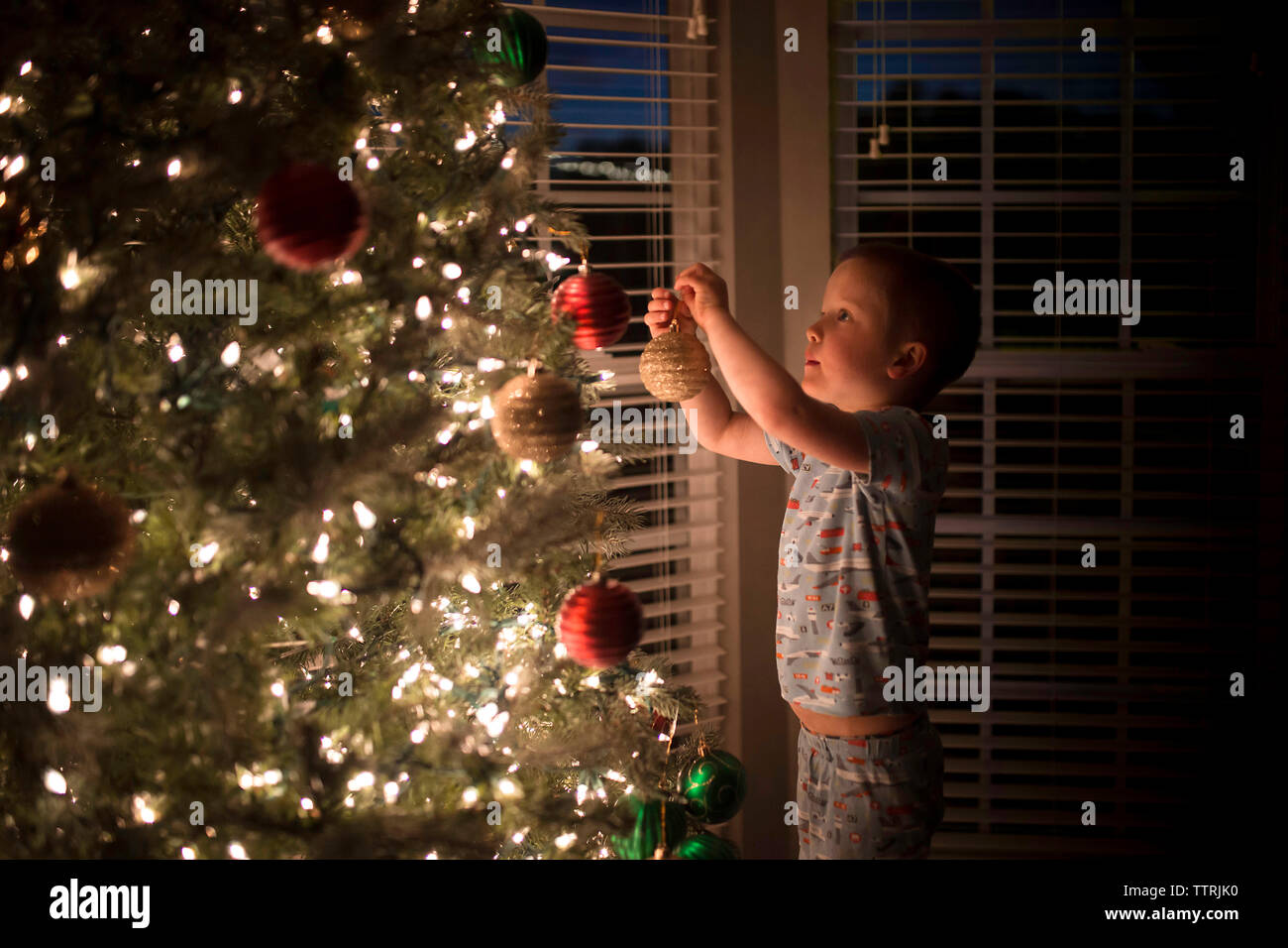 Side view of boy hanging bauble on illuminated christmas Tree at home Stock Photo