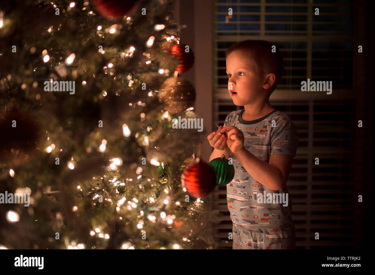Boy holding bauble while looking at illuminated christmas Tree Stock Photo