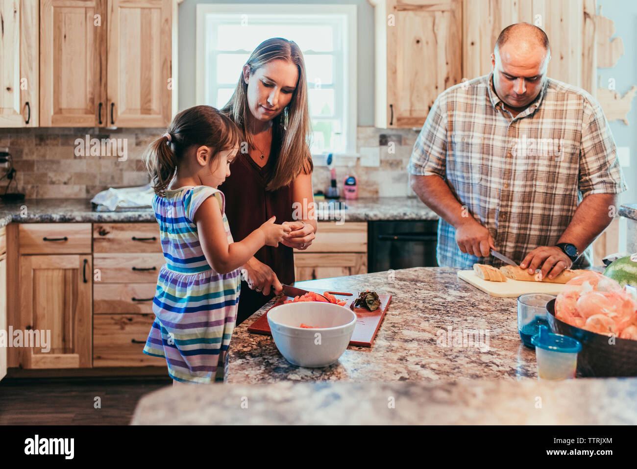 Parents preparing food while standing with daughter in kitchen at home Stock Photo