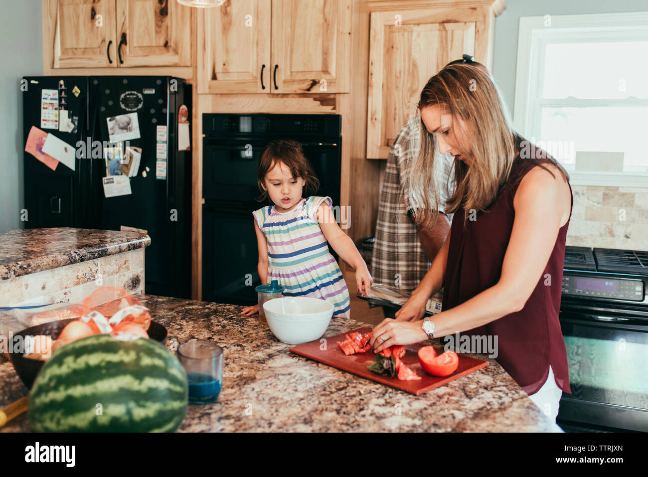 Daughter standing by parents preparing food in kitchen at home Stock Photo
