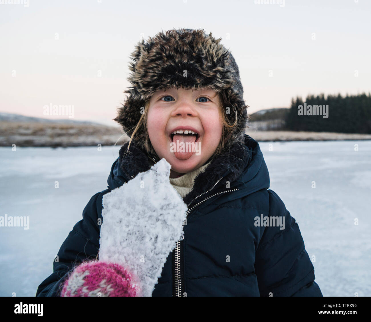 Portrait of playful girl sticking out tongue while holding ice during winter Stock Photo
