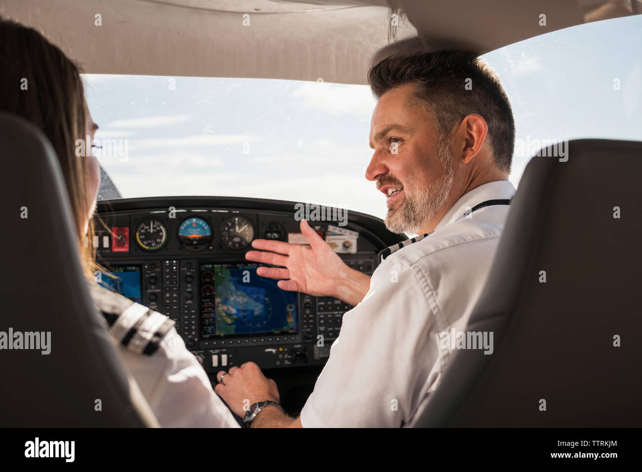Rear view of male pilot teaching female trainee to operate control panel in airplane at airport Stock Photo