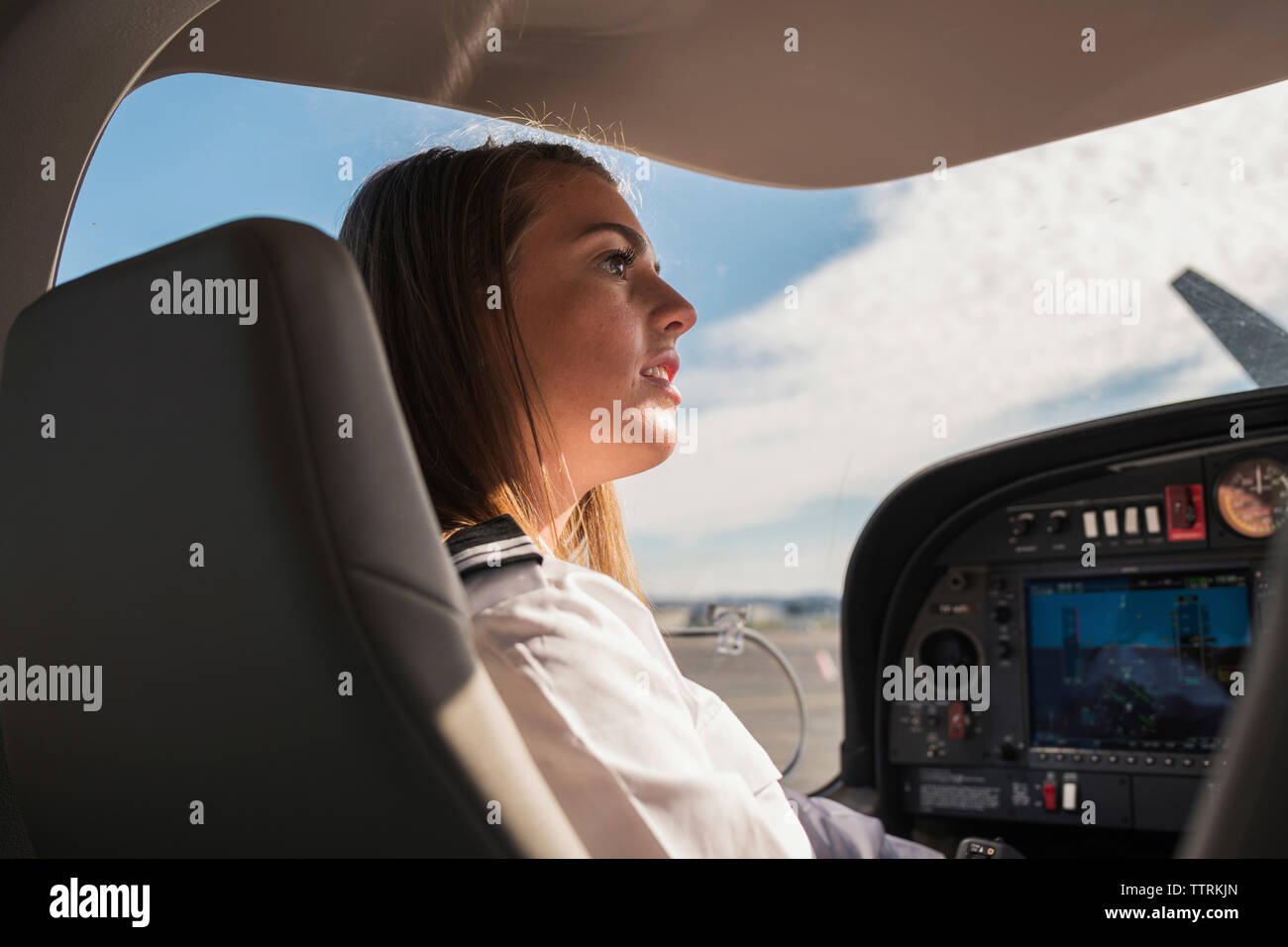 Side view of female pilot looking away while sitting in airplane at airport Stock Photo