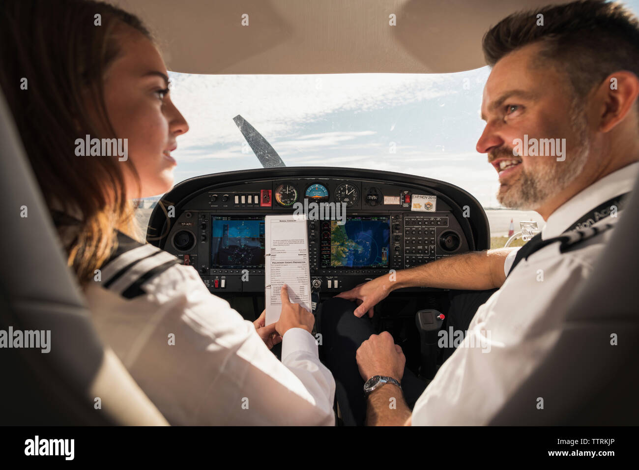 Rear view of female trainee discussing paper with male pilot in airplane at airport Stock Photo