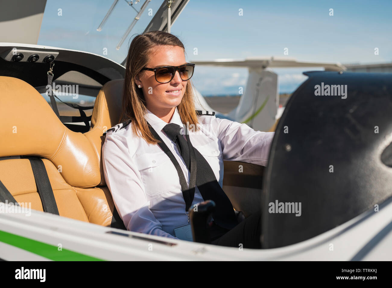 Confident female pilot wearing sunglasses sitting in airplane against ...