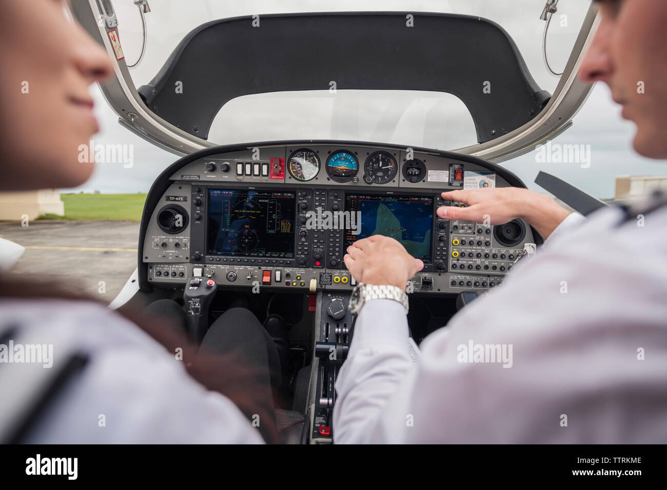 Cropped image of male pilot showing dashboard to female trainee while sitting in airplane at airport Stock Photo