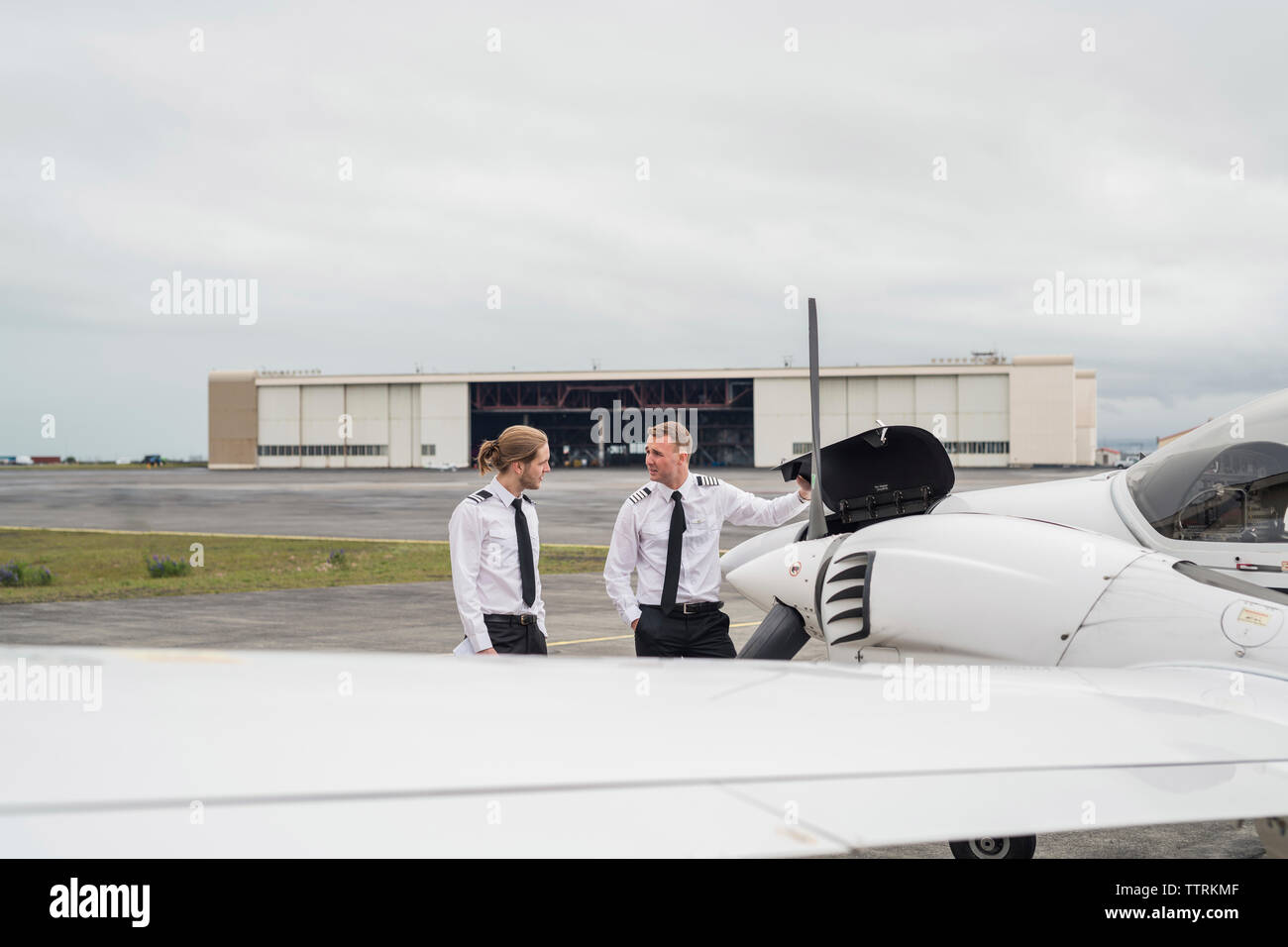 Engineer showing airplane parts to male trainee while standing against cloudy sky on airport runway Stock Photo