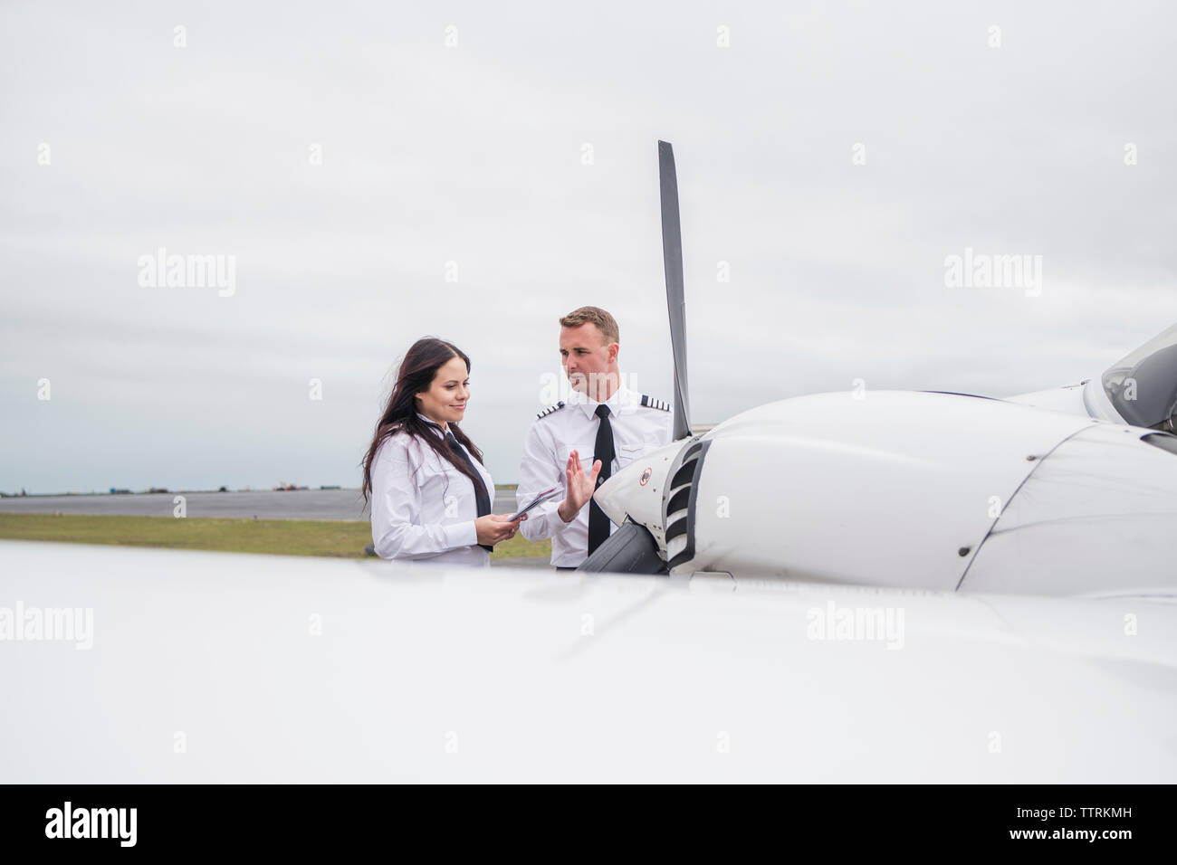 Engineer showing airplane parts to female trainee while standing against cloudy sky on airport runway Stock Photo