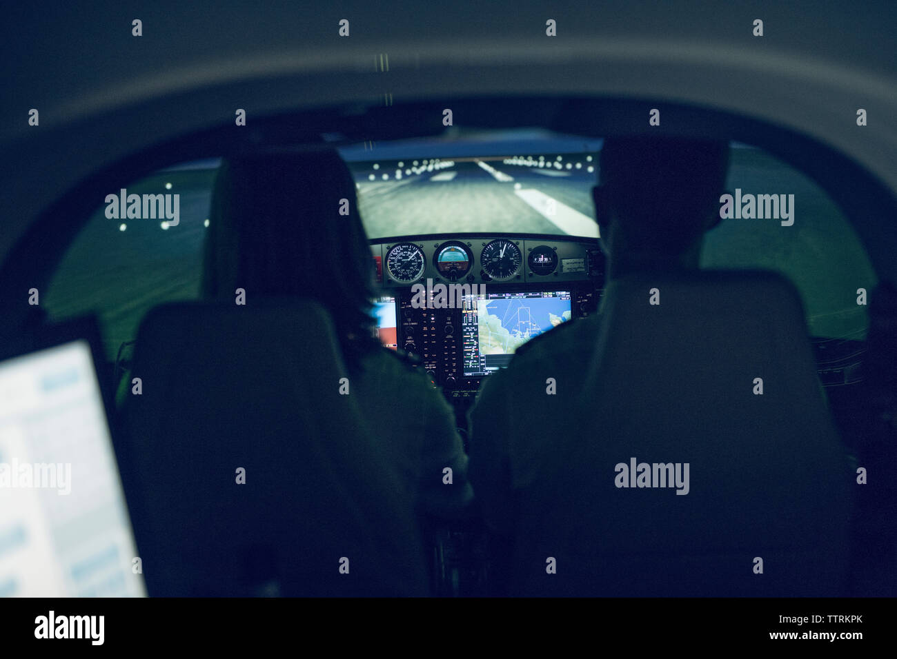 Rear view of silhouette pilot giving training to male trainee in flight ...