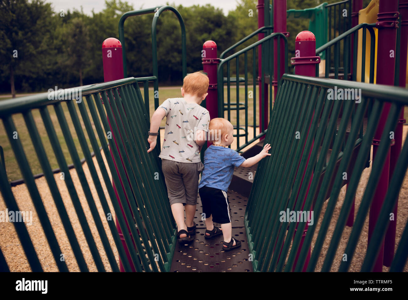 Rear view of brothers walking on jungle gym at playground Stock Photo