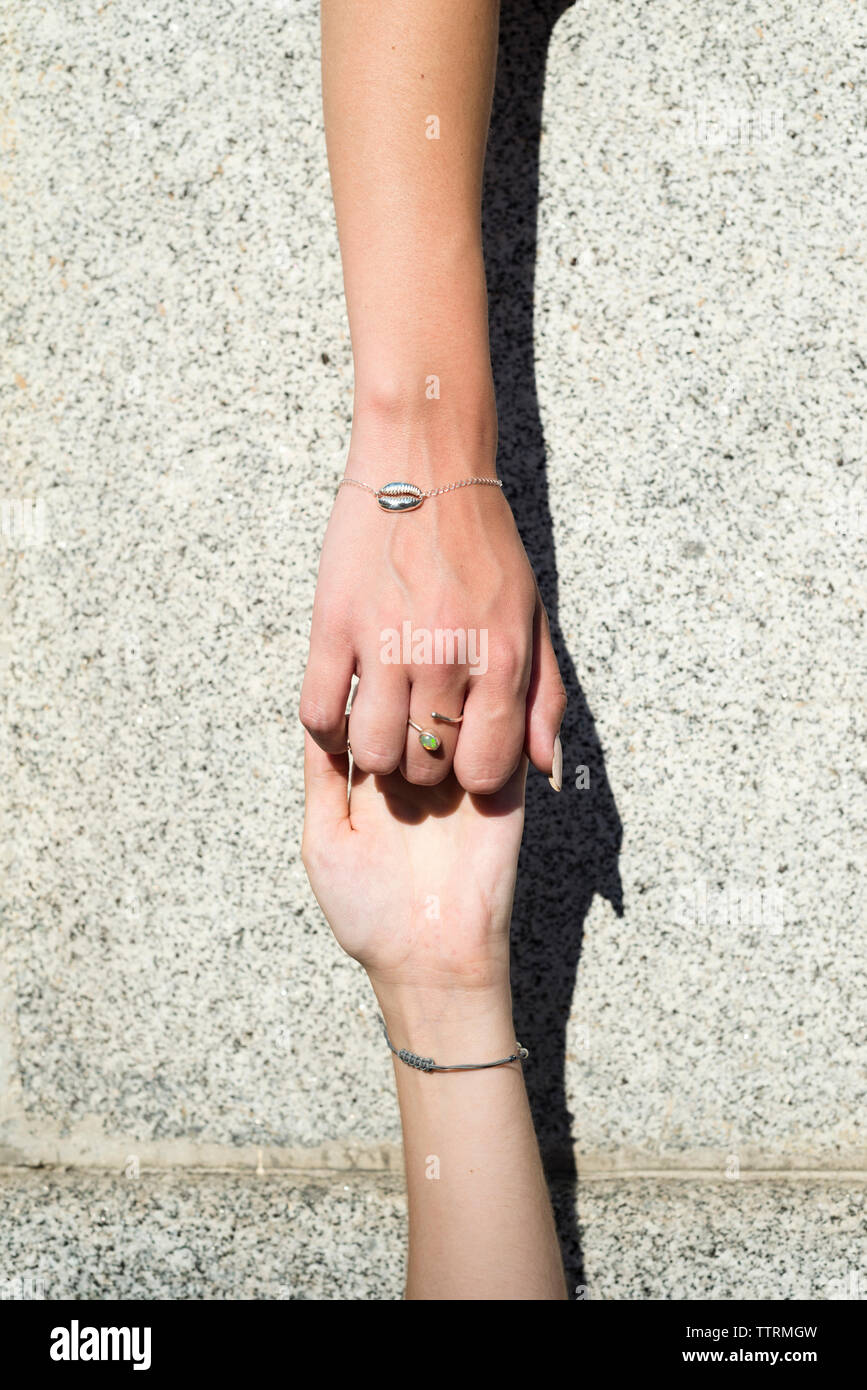 cropped image of friends wearing bracelets holding hands by wall during sunny day TTRMGW