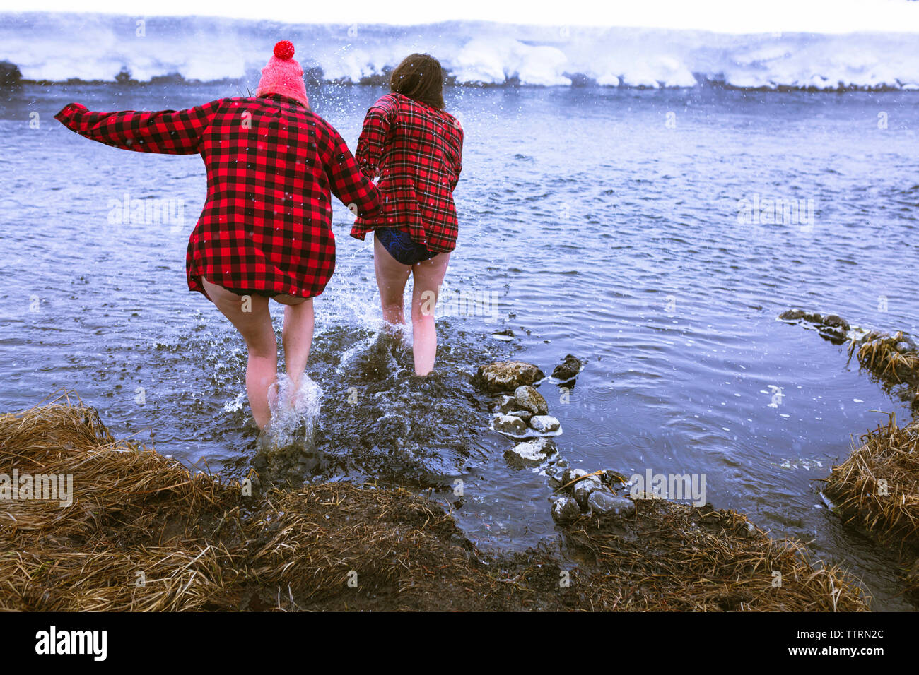 Rear view of female friends enjoying in lake during winter Stock Photo