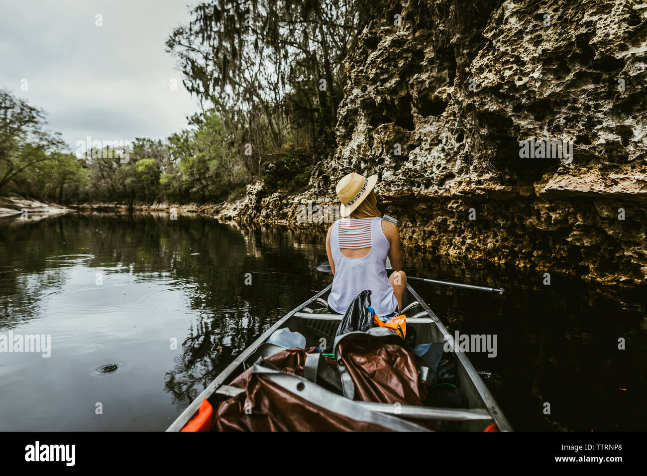 Rear view of young woman wearing hat while canoeing in lake at forest Stock Photo