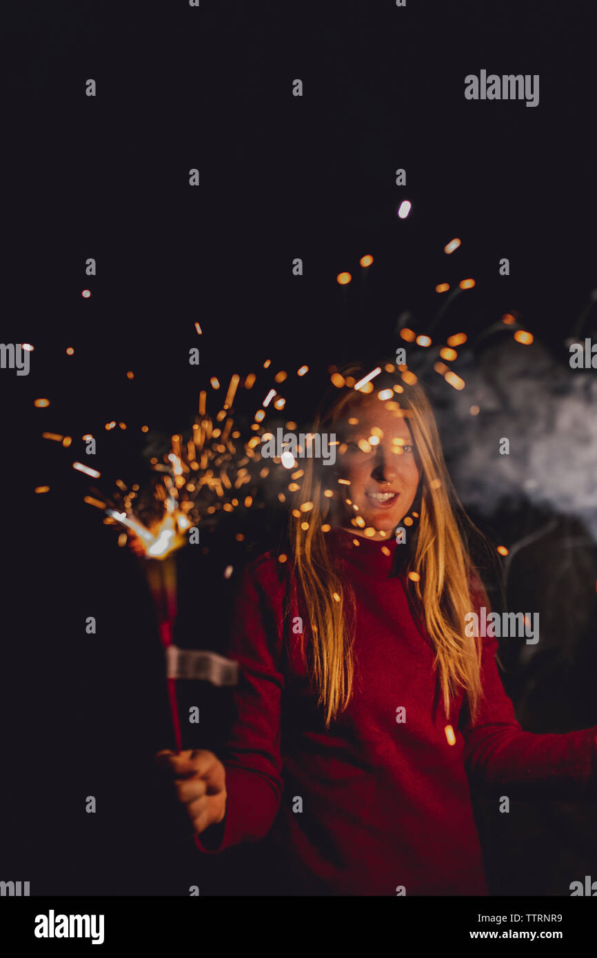 Portrait of woman burning firework while standing against sky at night Stock Photo
