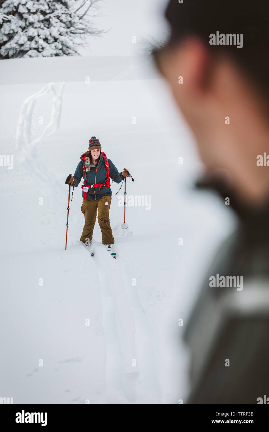young female skier heads down a hill as boyfriend watches Stock Photo