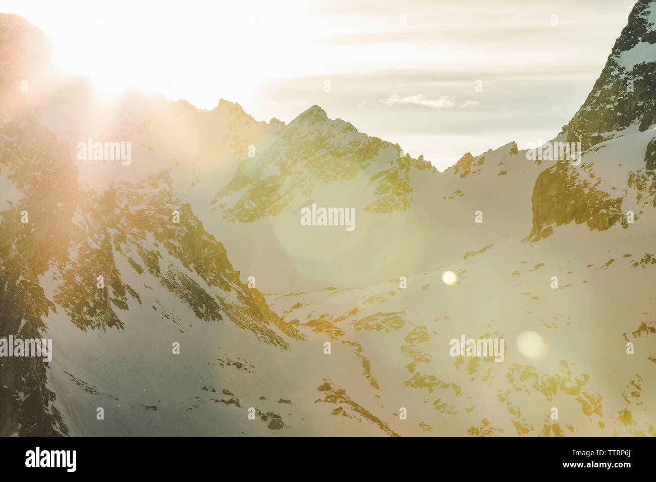 snowy mountains and sun flare at sunset on craggy ridgeline Stock Photo