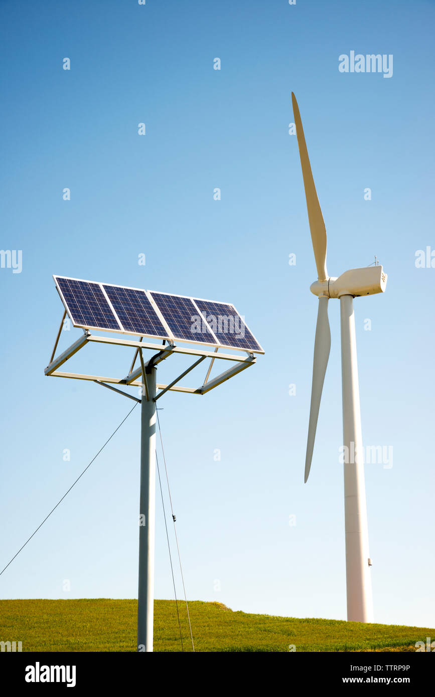 Wind turbine and solar panels on field against clear sky Stock Photo