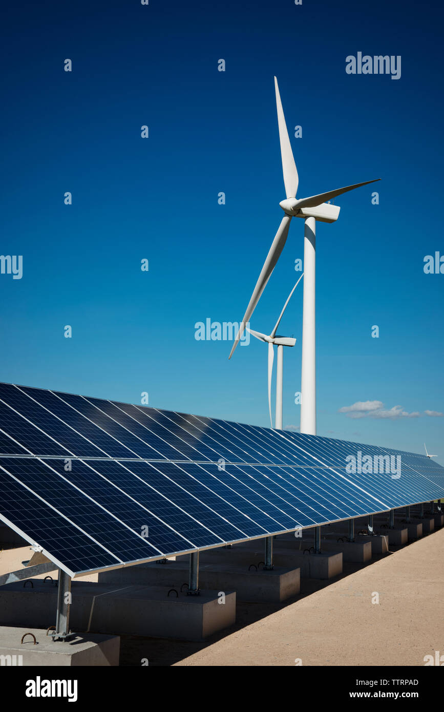 Solar panels on factory by windmills against blue sky Stock Photo