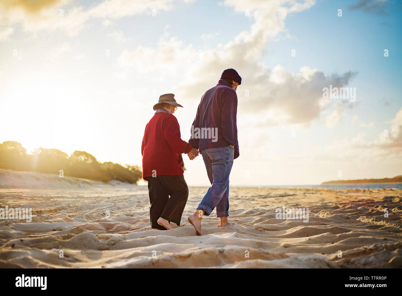 Senior couple holding hands while walking on sandy beach on sunny day Stock Photo