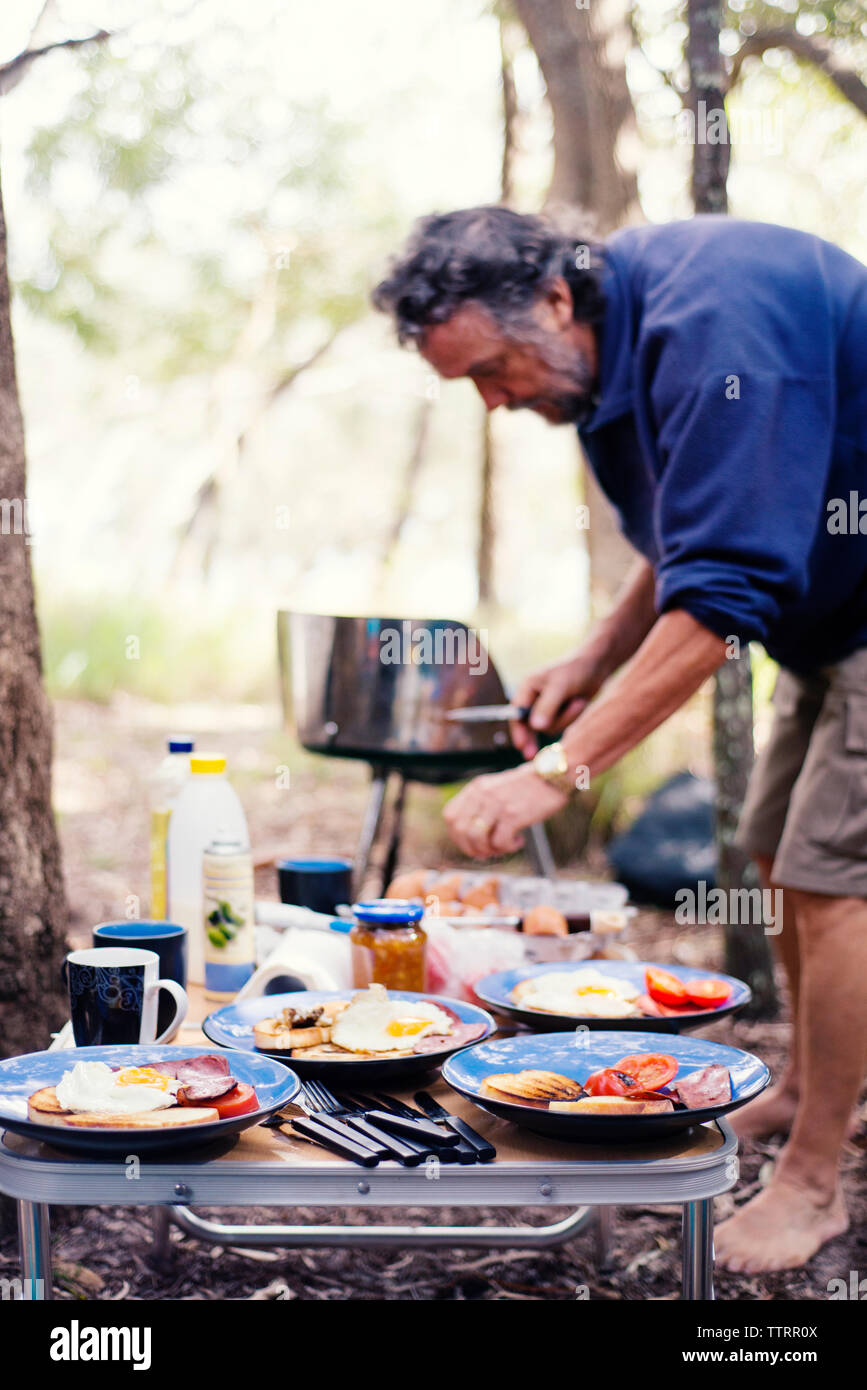 Side view of senior man preparing food in forest Stock Photo