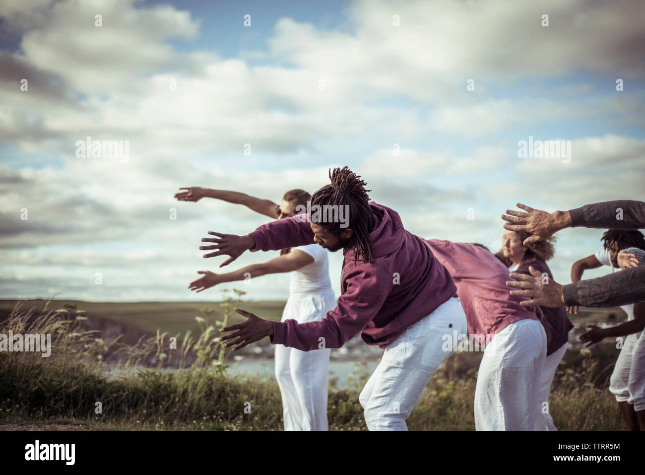 People practicing relaxation exercise on field against cloudy sky Stock Photo
