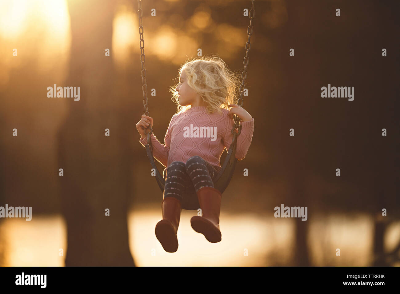 Girl playing on swing at playground during sunset Stock Photo - Alamy