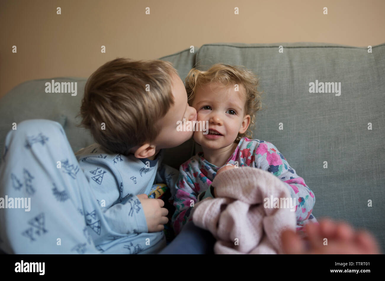 Boy kissing sister while sitting on sofa at home Stock Photo