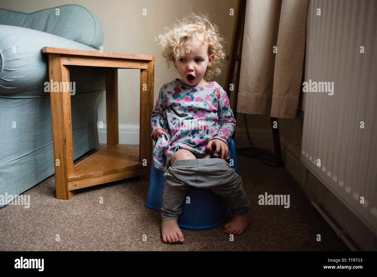 Girl with mouth open sitting on potty in room at home Stock Photo