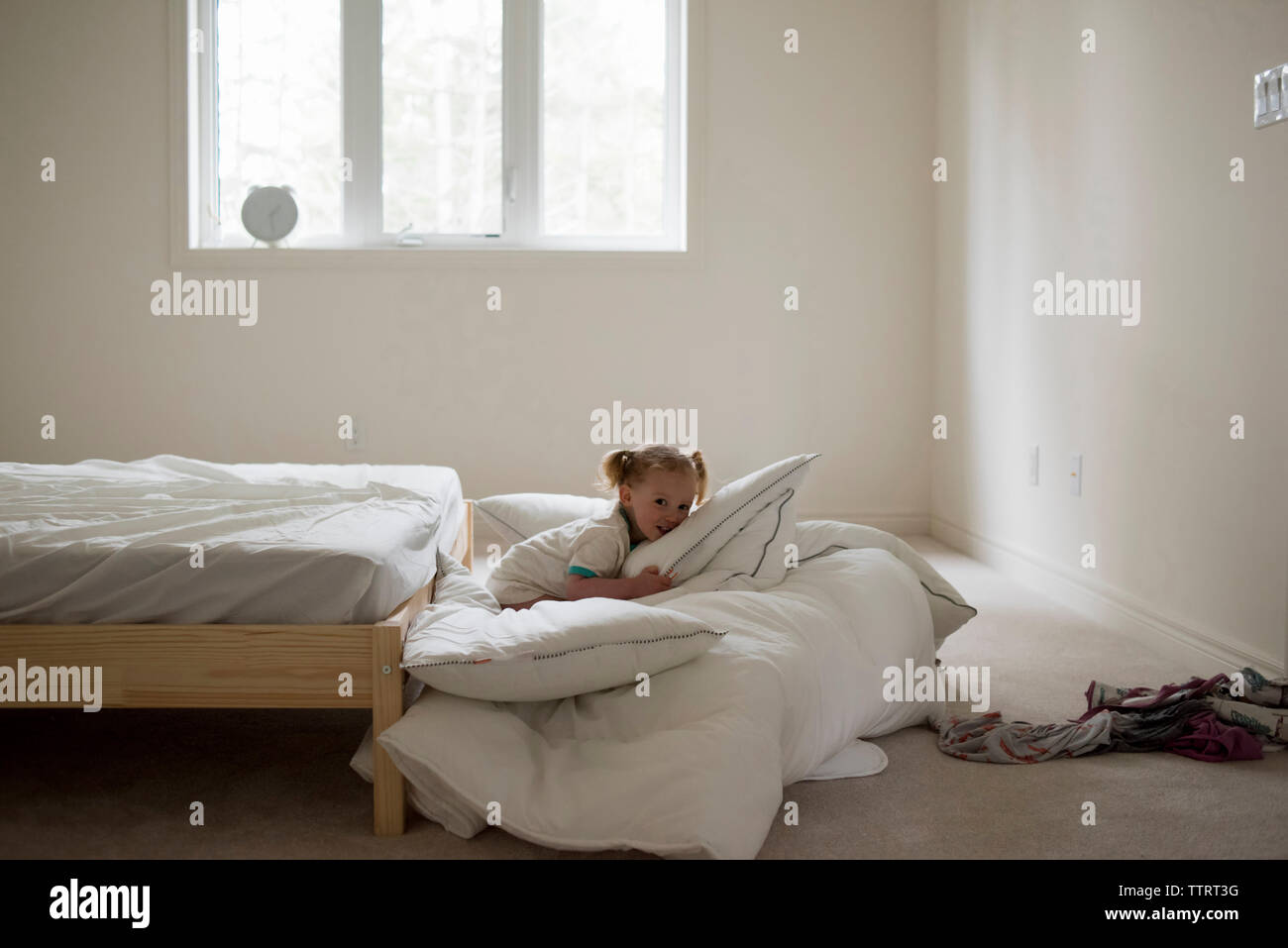 Portrait of girl sitting on duvet by bed in bedroom Stock Photo