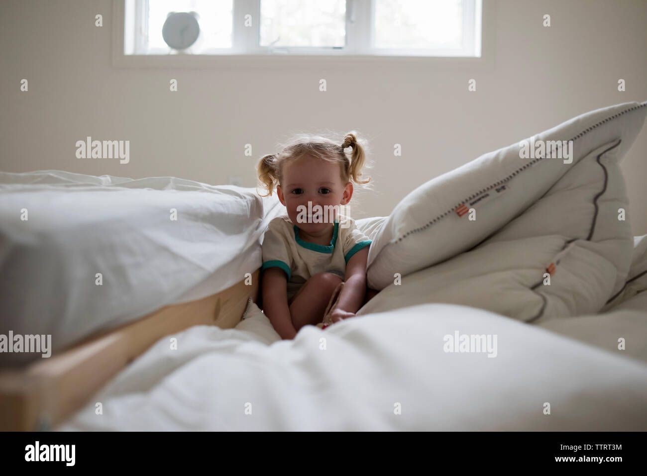 Portrait of smiling girl sitting on duvet by bed at home Stock Photo