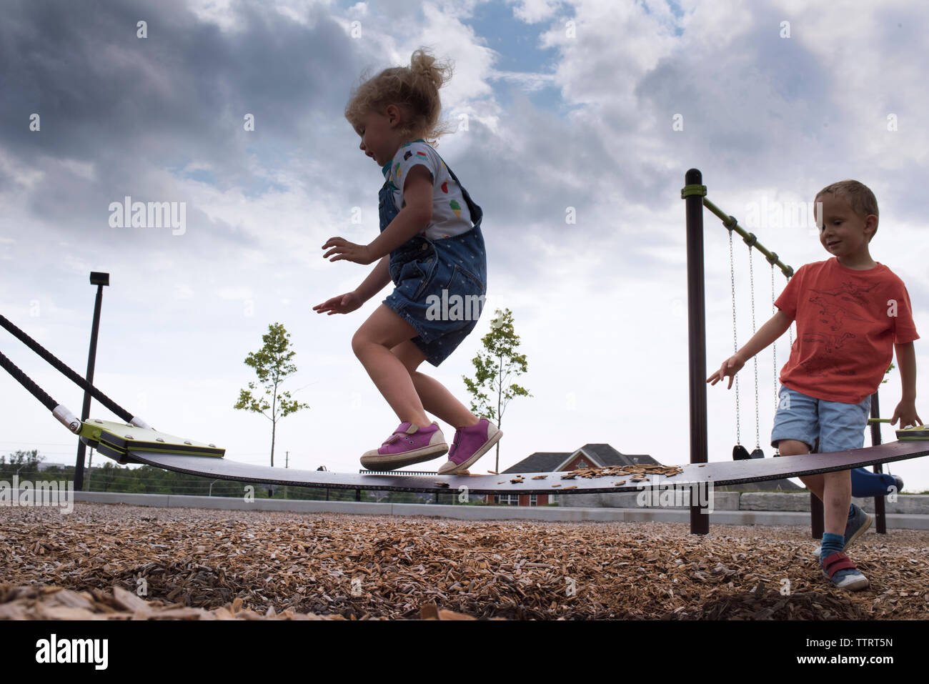 Low angle view of siblings playing on outdoor play equipment at playground against storm clouds Stock Photo