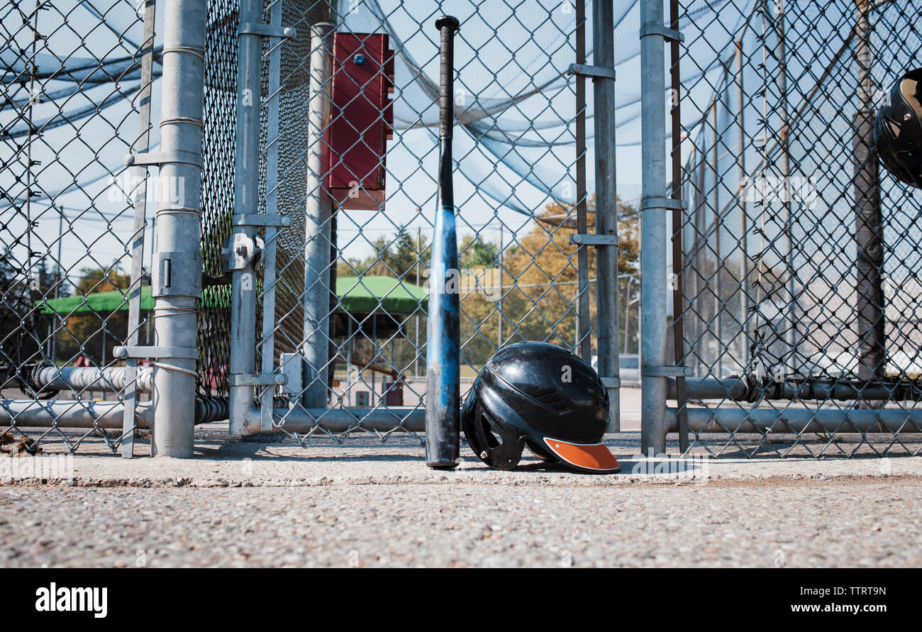 Baseball bat and sports helmet against chainlink fence at playing field during sunny day Stock Photo