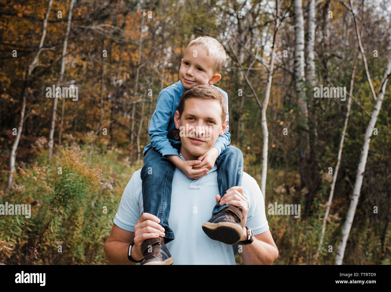 Portrait of father carrying son on shoulders while standing in forest Stock Photo