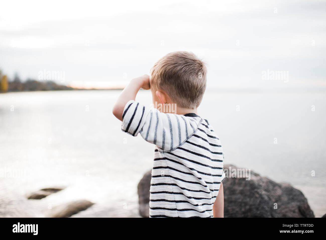 Side view of boy standing by Lake Simcoe against cloudy sky Stock Photo
