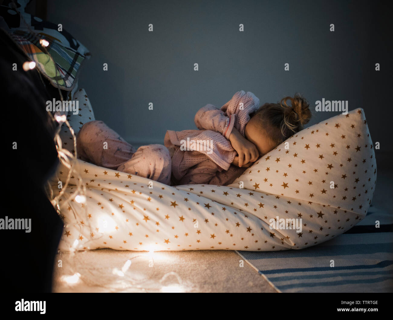 Girl sleeping by illuminated string lights on bed at home Stock Photo