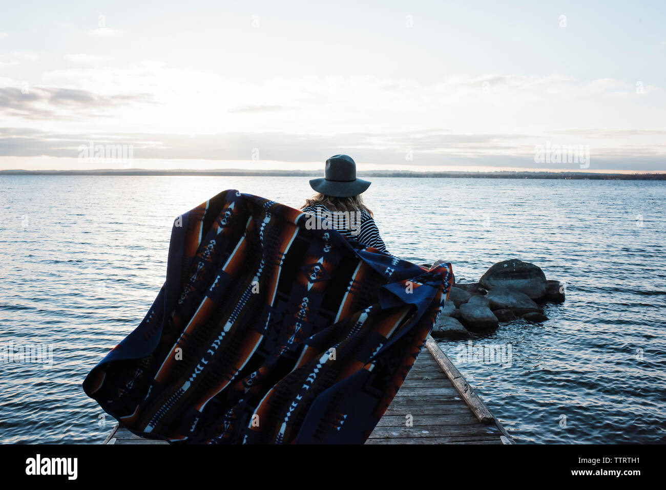 Rear view of woman with blanket standing on pier by Lake Simcoe against sky Stock Photo