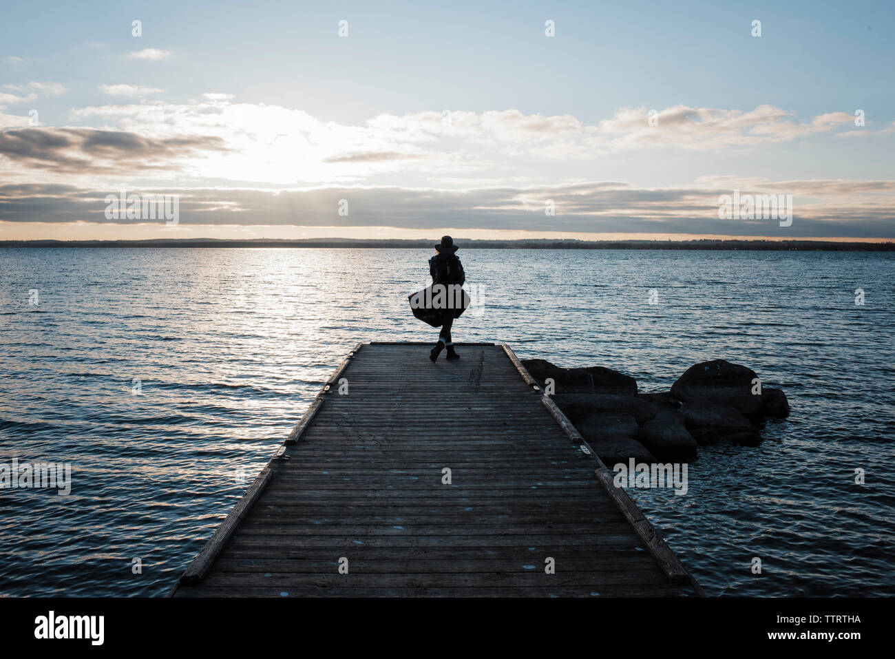 Rear view of woman wrapped in blanket standing on pier by Lake Simcoe against sky during sunset Stock Photo