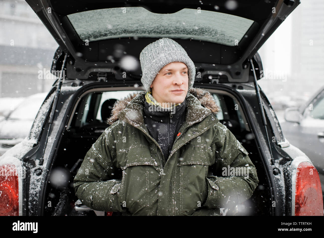 Man looking away while standing by car trunk during snowfall Stock Photo