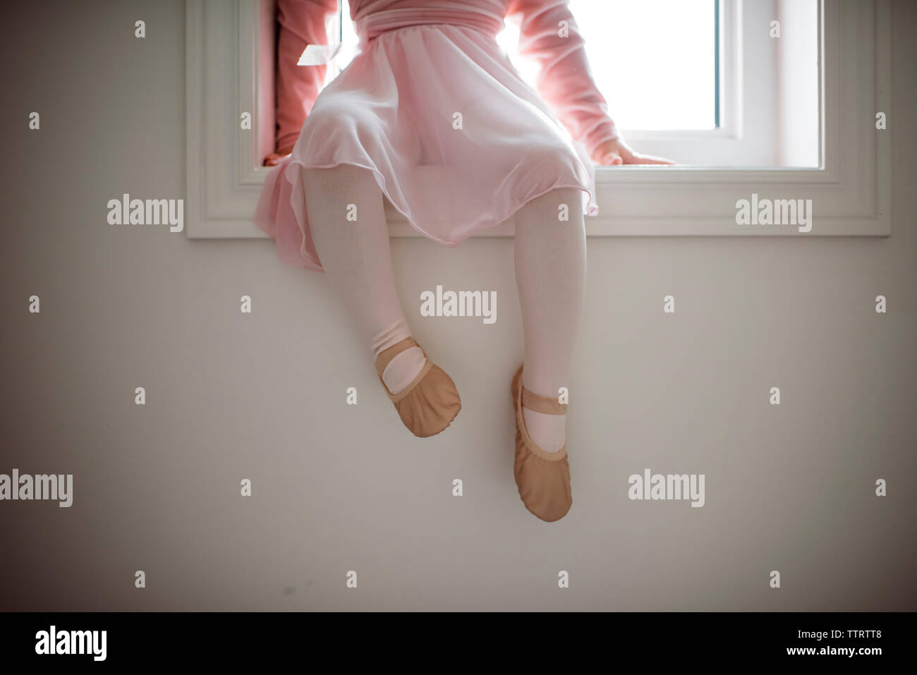 Low section of girl in ballet costume sitting on window sill at home Stock Photo