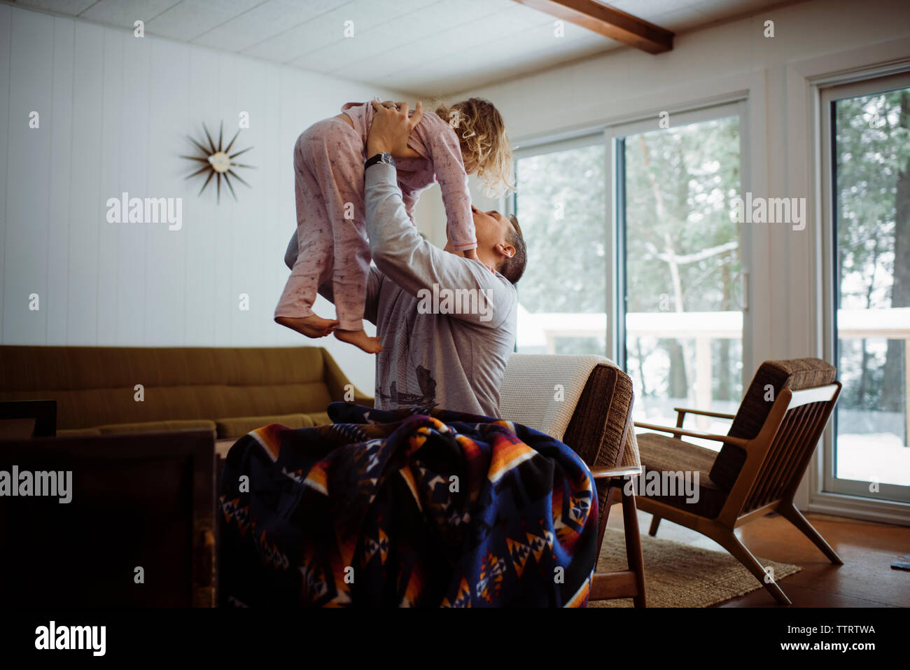 Father picking up daughter while sitting on chair at home Stock Photo