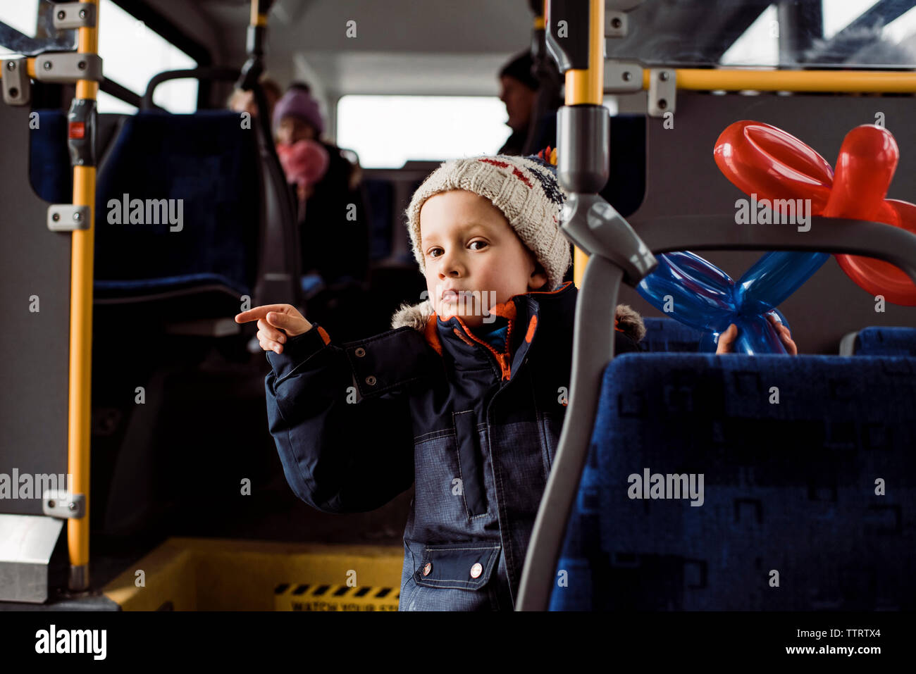 Cute boy with balloons wearing warm clothing while pointing in bus Stock Photo