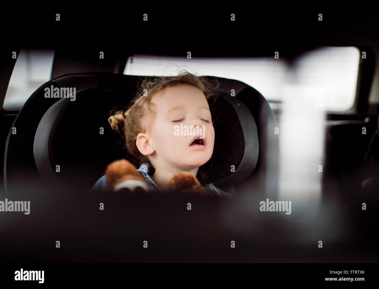Cute girl with mouth open sleeping in car seen through vehicle seat Stock Photo